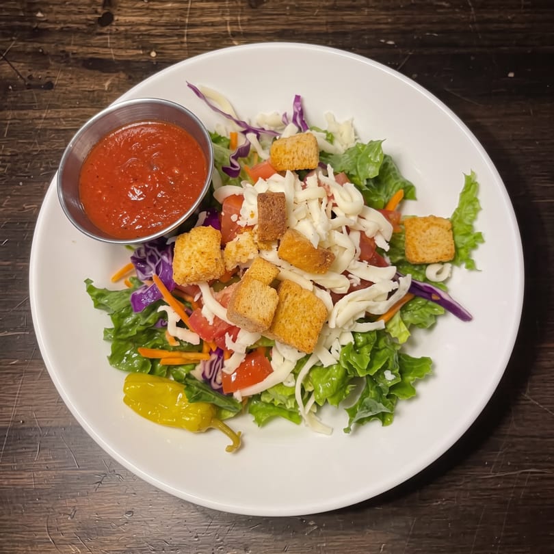 Fresh garden salad with mixed greens, cheese, croutons, tomatoes, and a side of red dressing.