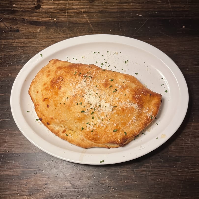 Golden-brown calzone topped with grated cheese and herbs on a white plate.
