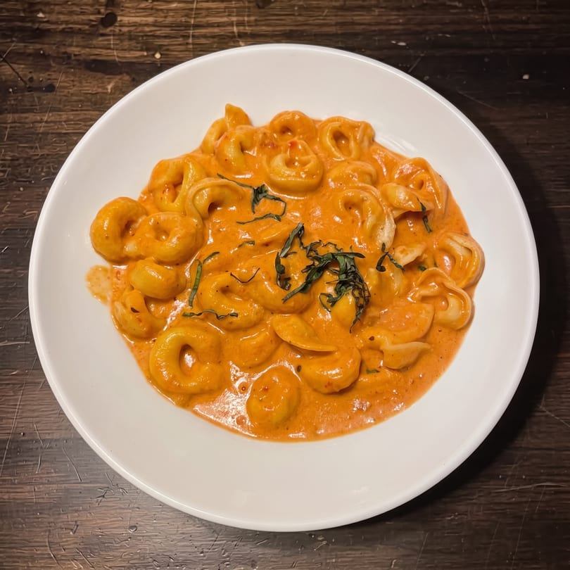 Tortellini pasta in a creamy orange sauce, garnished with fresh basil, served in a white bowl.