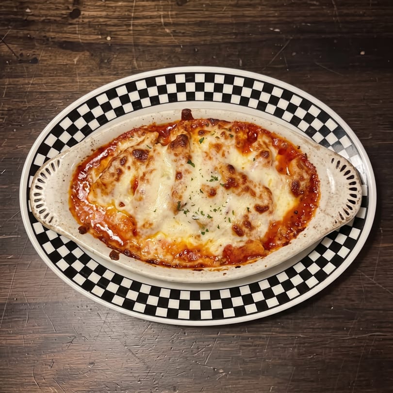 Cheesy baked pasta in red sauce, served in a white dish on a black and white checkered plate.